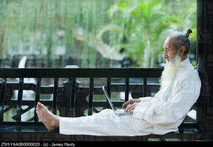 Elderly man in traditional Chinese clothing, barefoot, using laptop